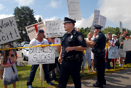 PORTSMOUTH, NH - AUGUST 11: Police stand near protesters outside Portsmouth High School where U.S President Barack Obama is holding a town hall August 11, 2009 in Portsmouth, New Hampshire. President Obama is in town to speak about the need for health insurance reform to a crowd of eighteen hundred. (Photo by Darren McCollester/Getty Images)